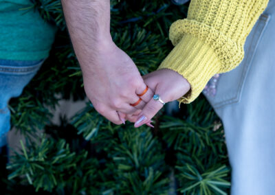 A couple holding hands showing off a thumb ring against the backdrop of faux pine garlands.