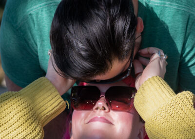 A dark-haired individual bending over the face of their partner with pink hair. Their partner has their hands up as they're looking up at them caressing their face with their fingers.