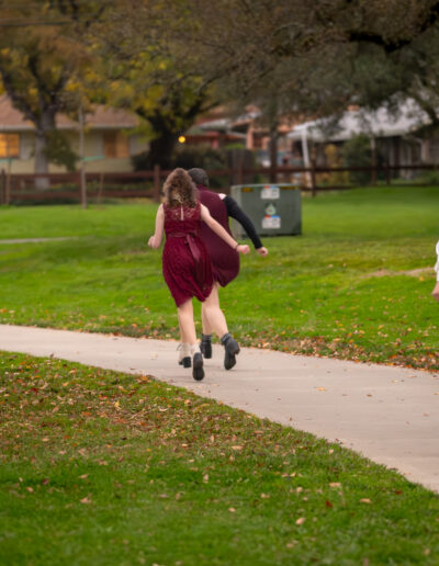 A picture from a park with a path curving from the bottom right to the middle left of the image. There are four kids running down the path away from the camera.