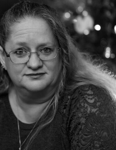 A black and white image of a woman leaning forward in front of a christmas tree, her hair lit from the back by the lights.